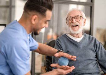 Joyous aged man undergoing a session of physical therapy conducted by an experienced rehabilitation doctor